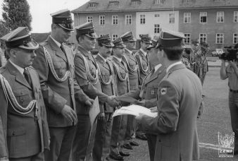 Fot. 84. Dowódca Pułku mjr Tadeusz Choiński wręcza dyplomy, asystuje kpt. Dariusz Arent. Na fotografii od lewej: pierwszy mjr Jacek Galas (dowódca batalionu czolgów) drugi  kpt. Maciej Dubil (szef służby mundurowej), trzeci kpt. Leszek Gluma (szef służby finansowej), czwarty kpt. Zbigniew Sobkowicz, piąty kpt. Dariusz Kowalski,szósty kpt. Krzysztof Marciniec, siódmy kpt Grzegorz Wilner. W tle fotografii, wychyla się z szeregu sierż. Andrzej Taborski . Uroczystość nagrywał sierż. Leszek Grocholski.